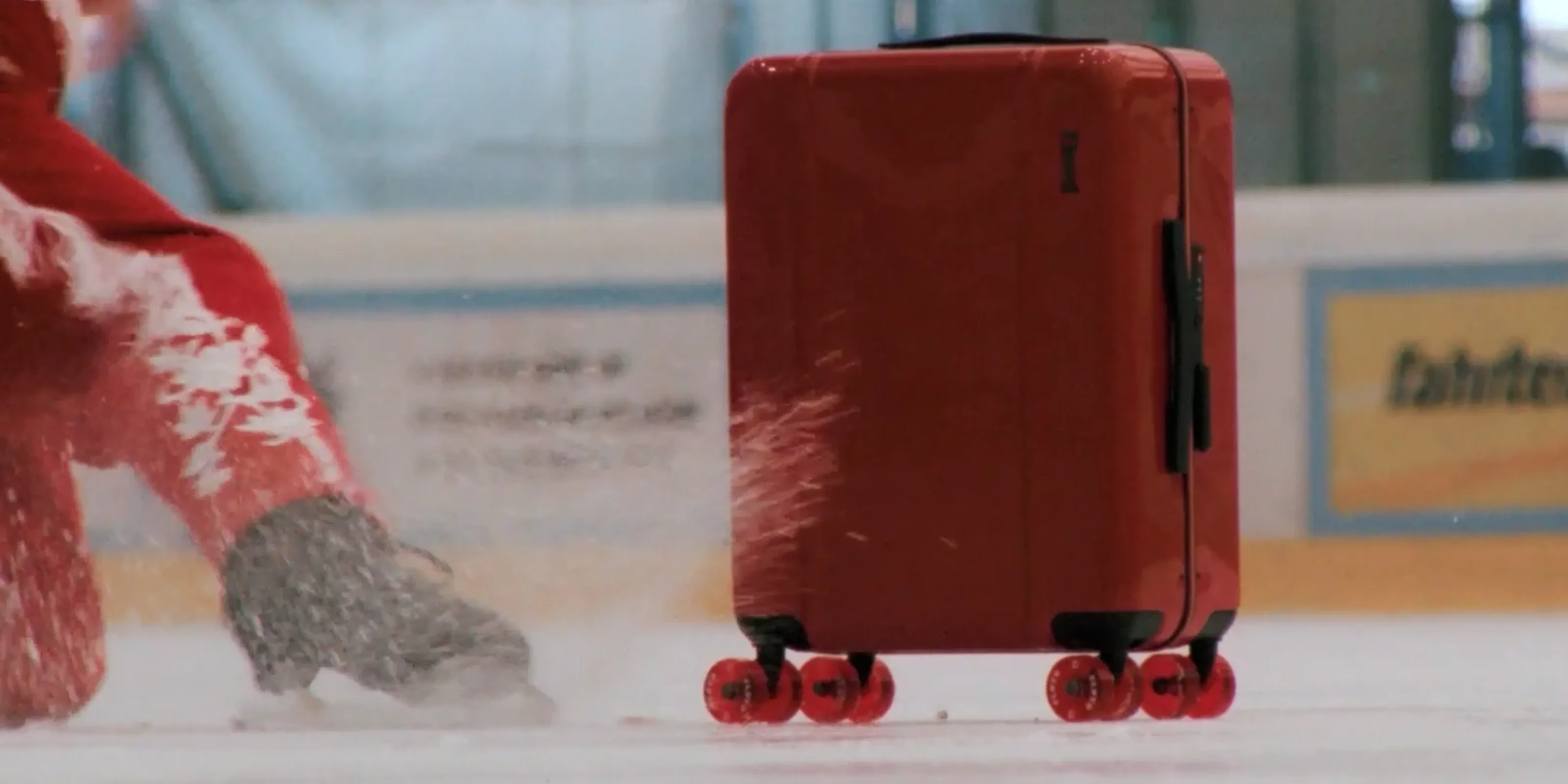 A red Floyd suitcase on the ice as the skater sprays snow beside it.