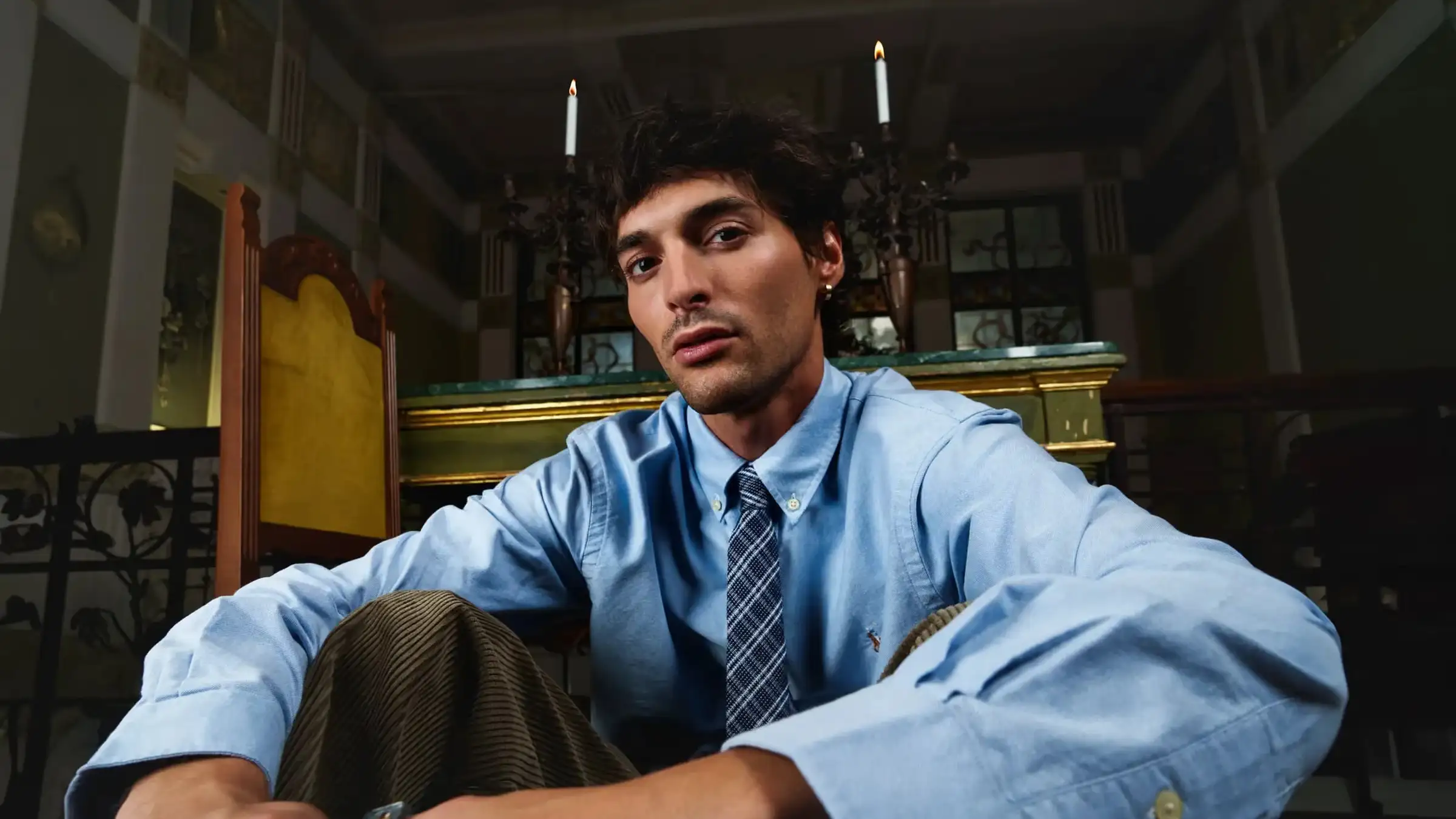 Male model in a blue shirt and tie seated in an ornate interior — MAXIMILIAN F/W campaign film by Studio ONOM.