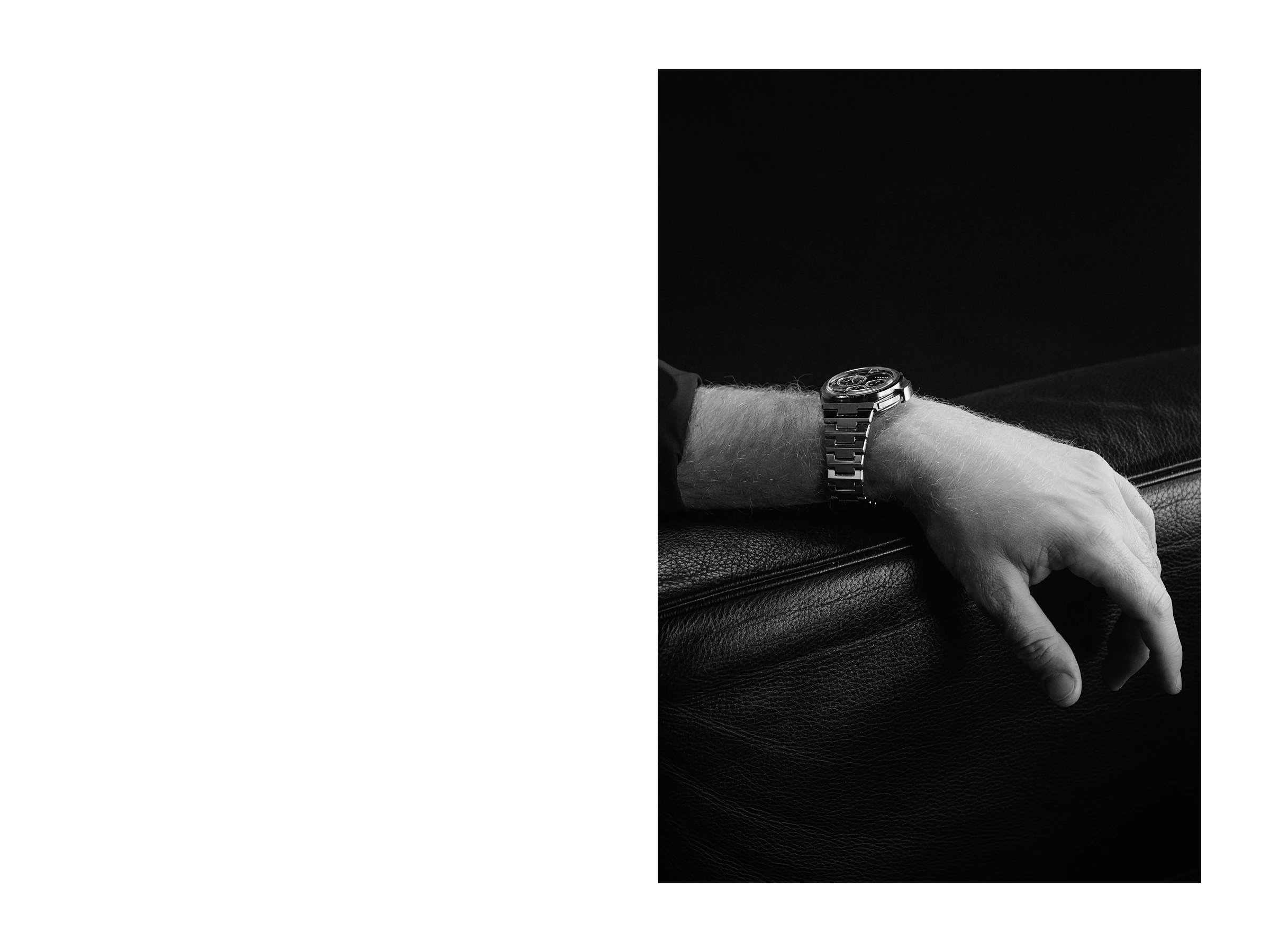 Hand resting on dark leather wearing the LÖBNER steel chronograph, low-key still life directed and produced by Studio ONOM