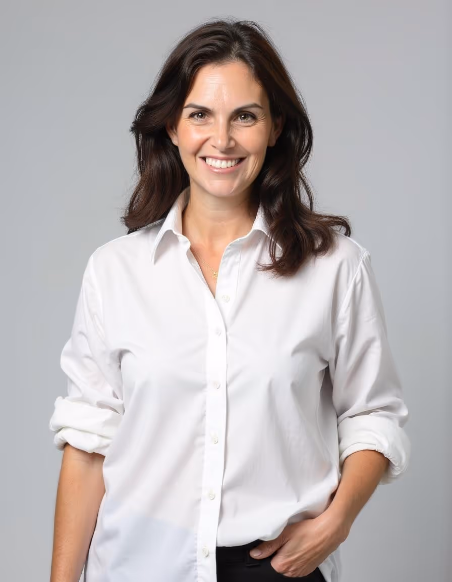 דנה ניסל, מחייכת ולבושה חולצה לבנה, עומדת מול רקע אפור ומביטה למצלמה