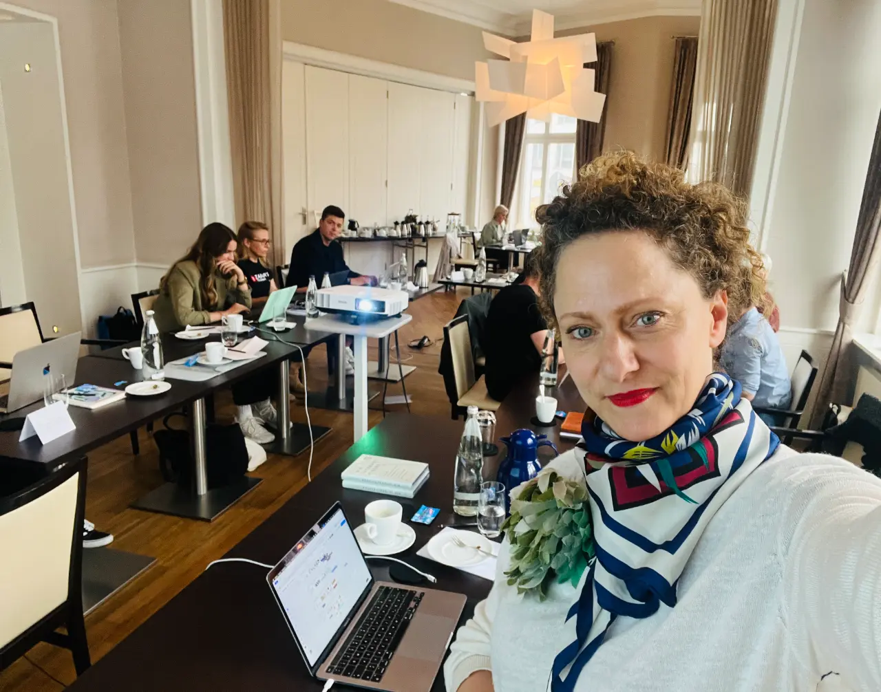 Julia Peglow macht Selfie während der CXI Masterclass in einem eleganten Konferenzraum mit Teilnehmern und Beamer
