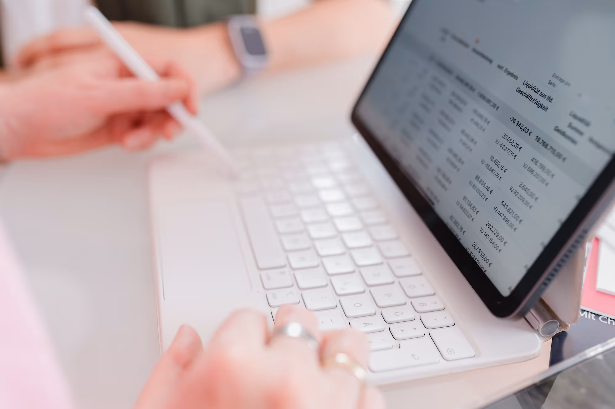 Person arbeitet an Tablet mit Tastatur und zeigt Finanzzahlen auf dem Bildschirm.