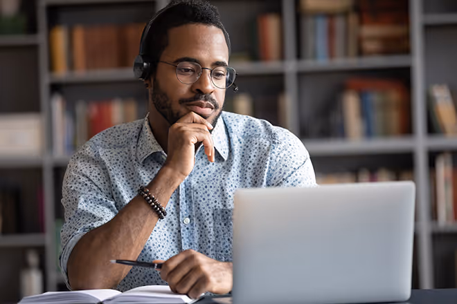 A man looks at his laptop pensively while taking notes.