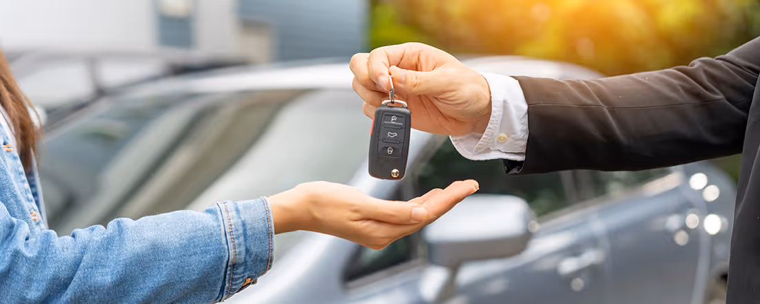 A car salesman hands a woman her new car keys.