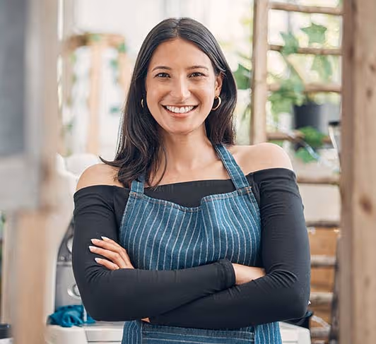A woman in an apron smiles with her arms crossed.