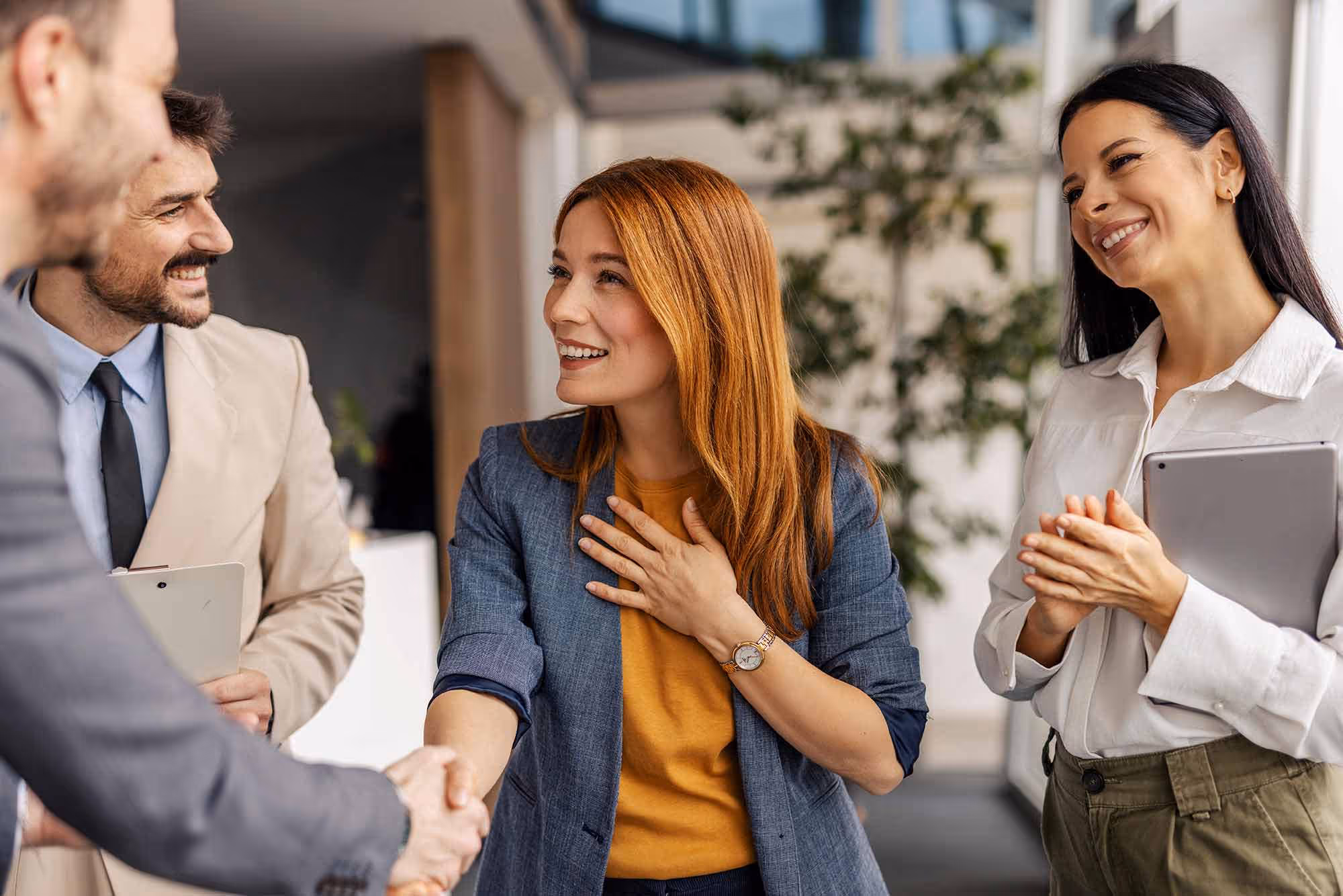 A group of people smiles at each other and shake hands in an office setting.