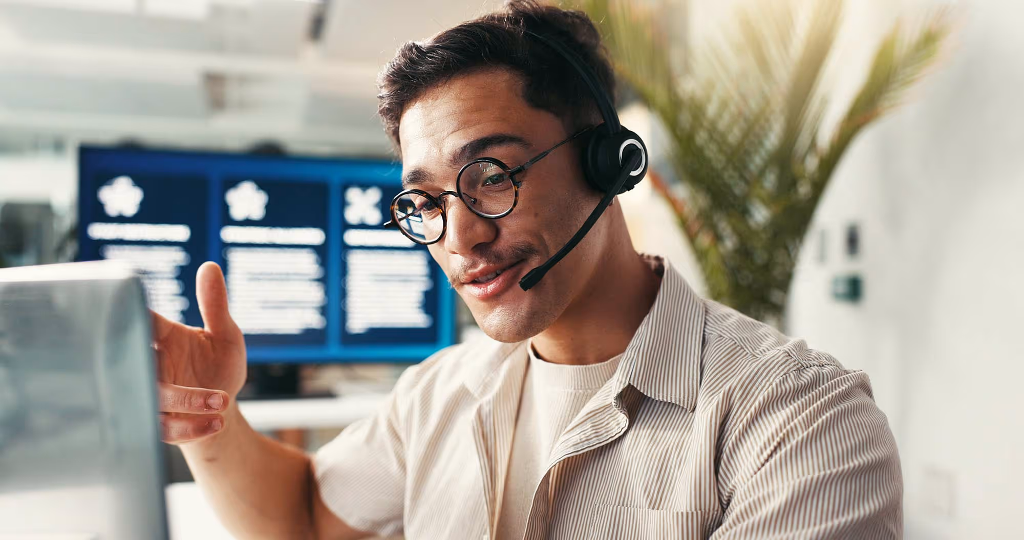 A young man talks into a headset in an office setting.