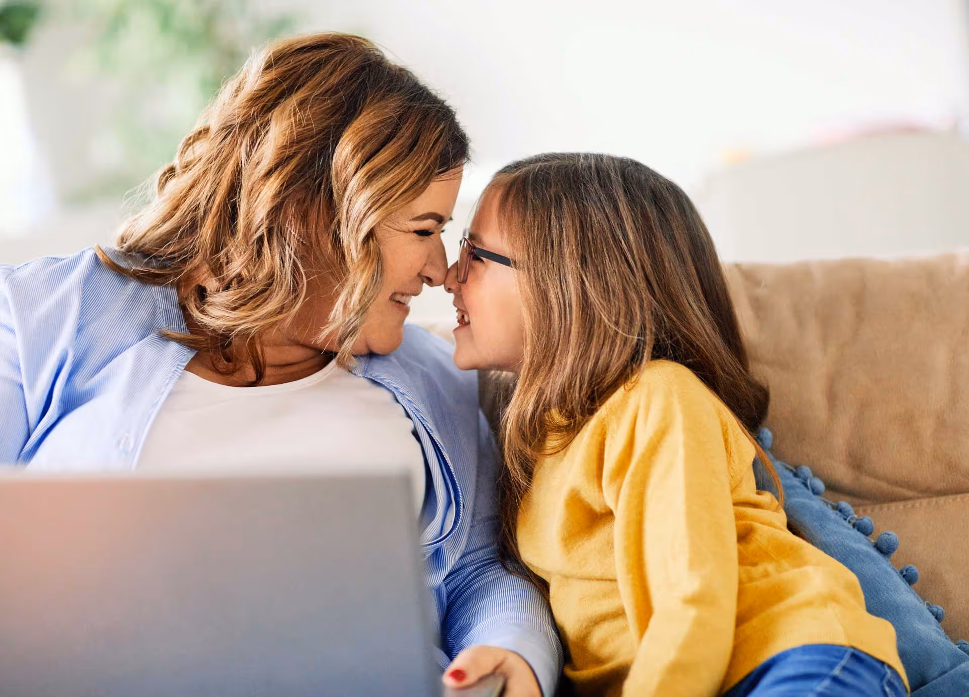 A mother and daughter touch noses  lovingly while using a laptop.