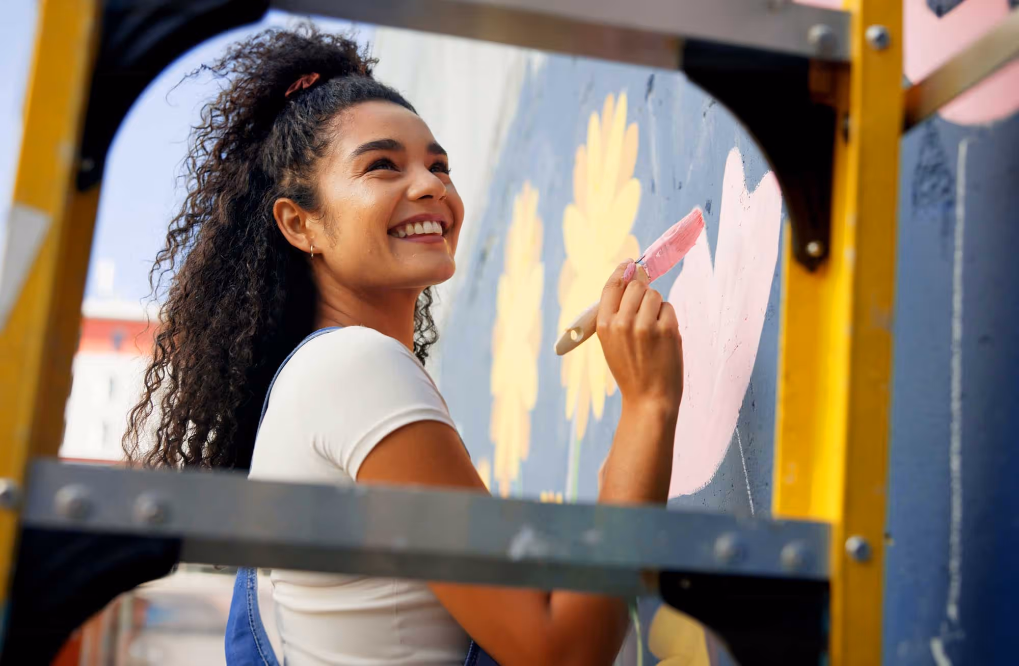 A young woman smiles while painting a mural.
