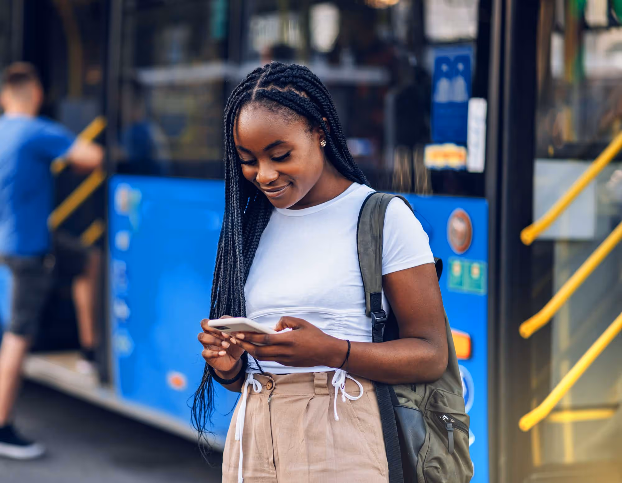 A young woman smiles while checking her phone in front of a bus.