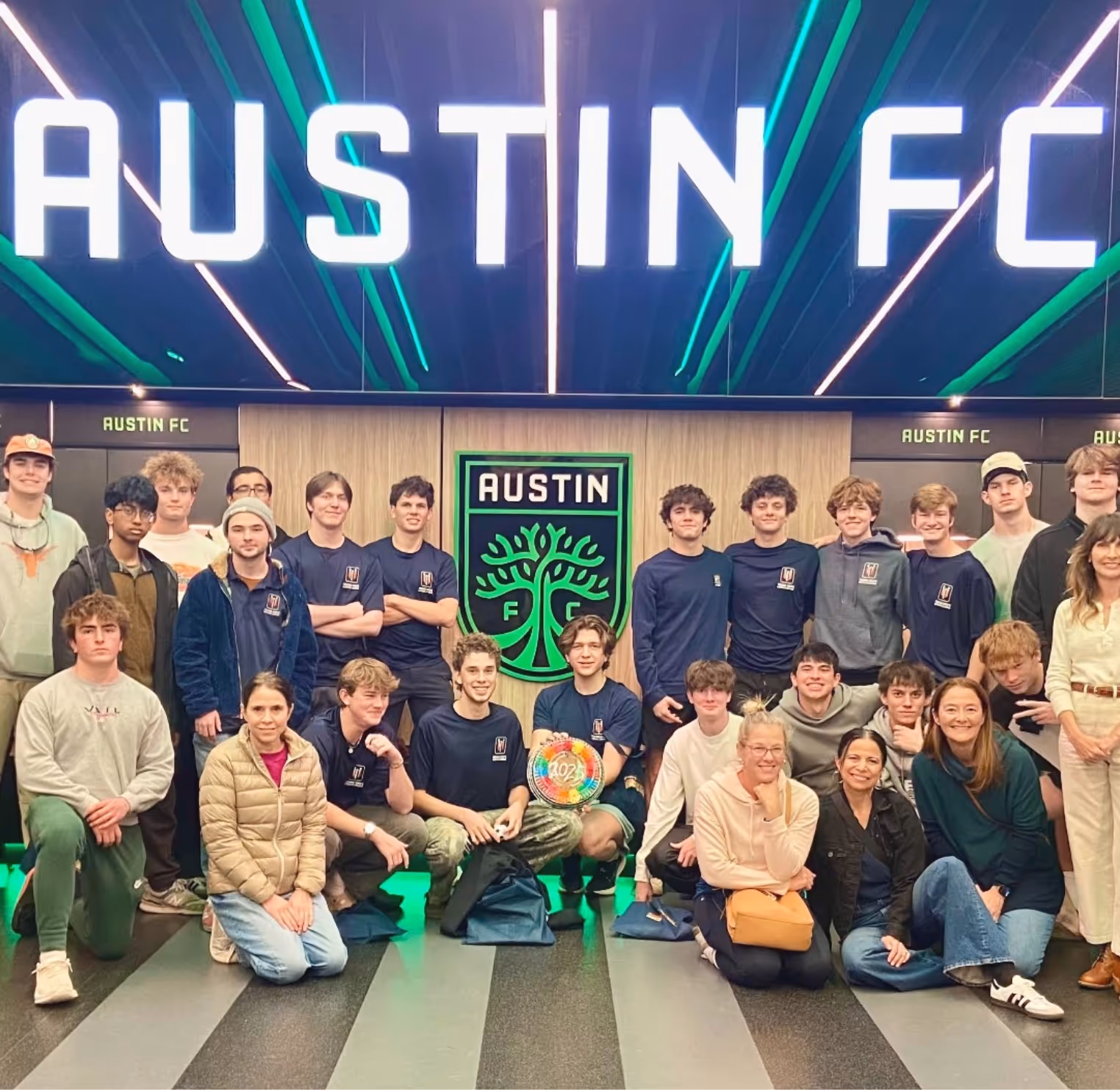 Group of young people and adults posing in front of an illuminated Austin FC logo and sign.