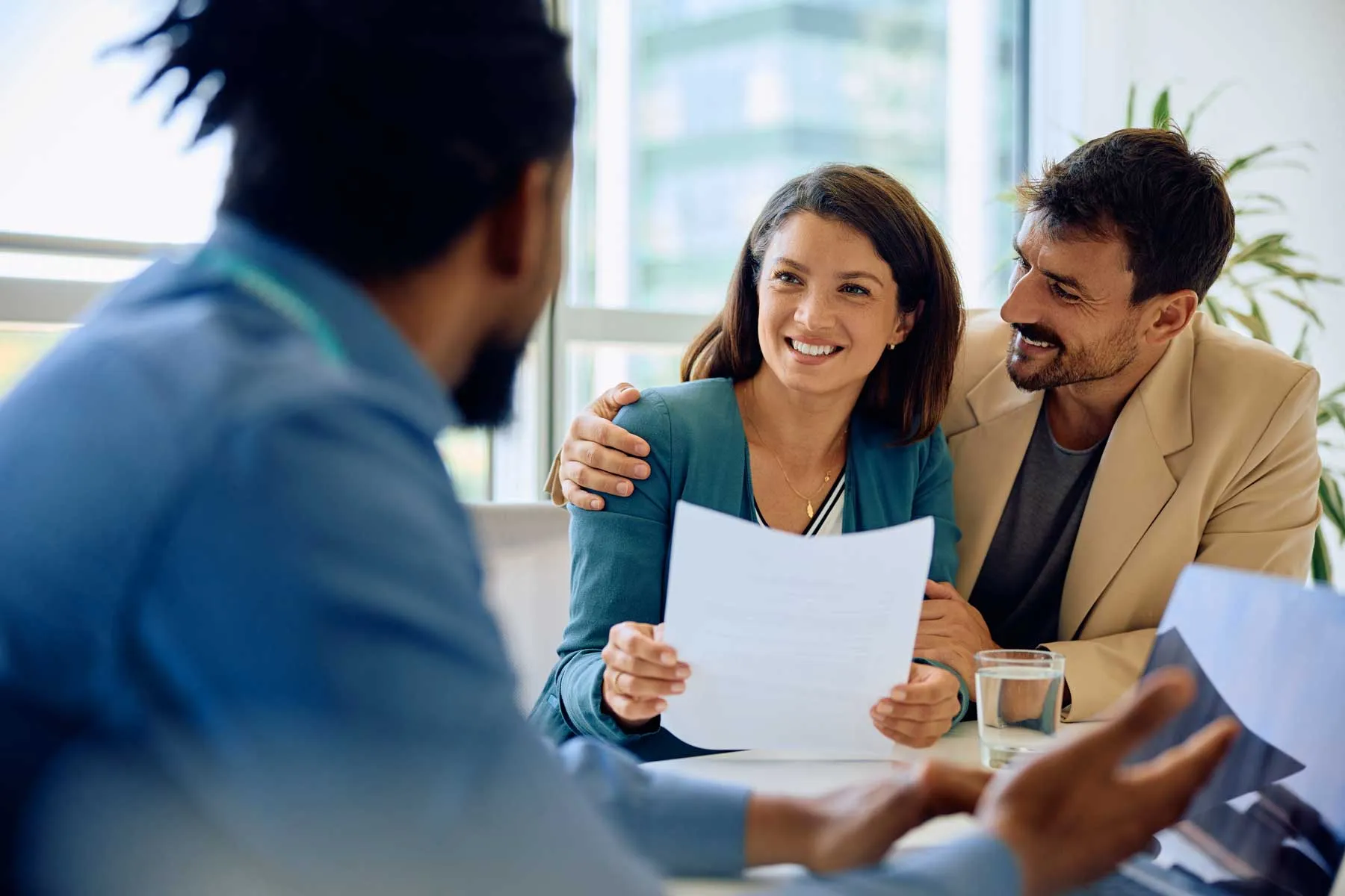 Smiling couple reviewing a document while talking with a professional in a bright office.