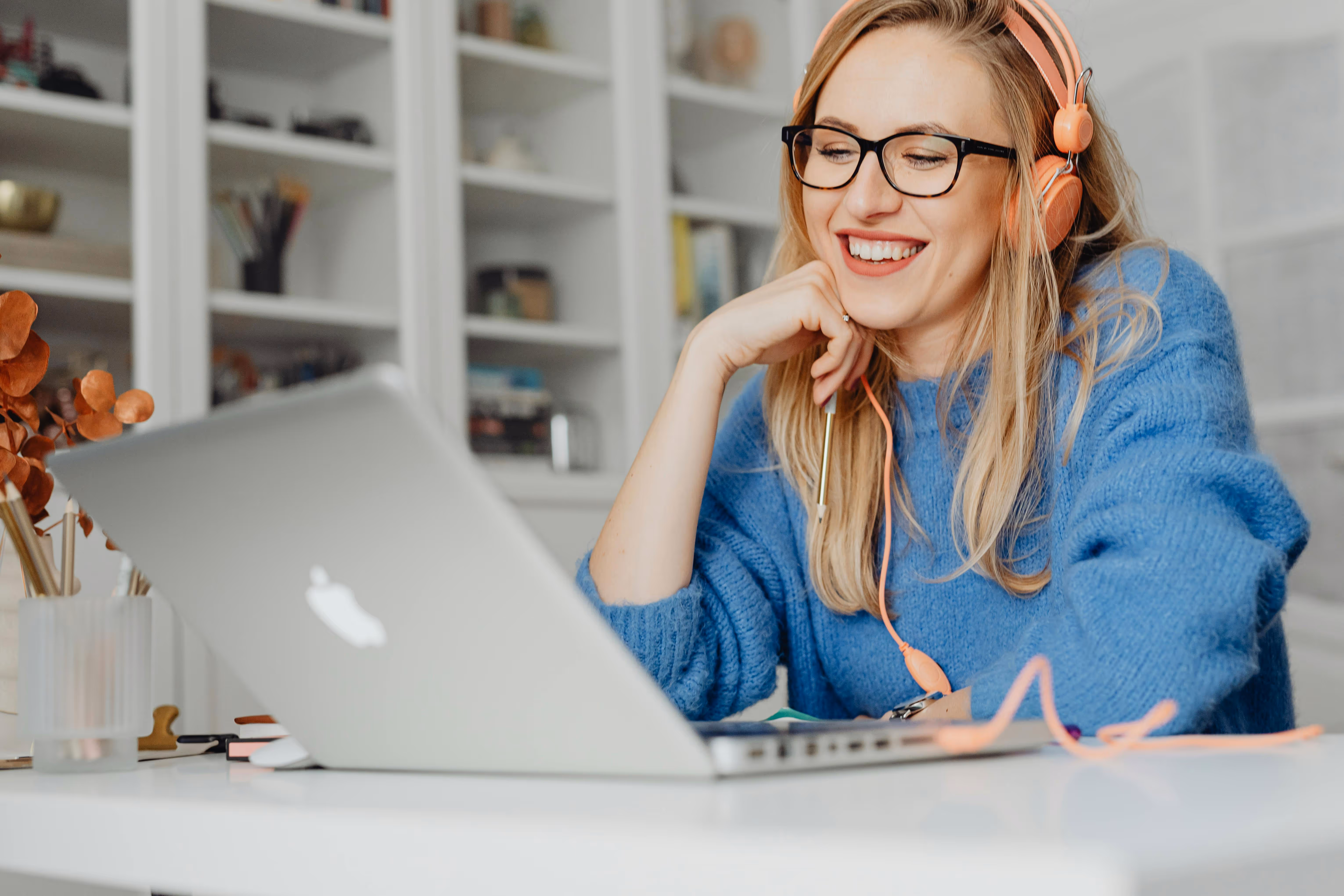 Smiling woman wearing orange headphones working on a laptop at a bright desk, representing a joyful, modern professional experience with Plannery.
