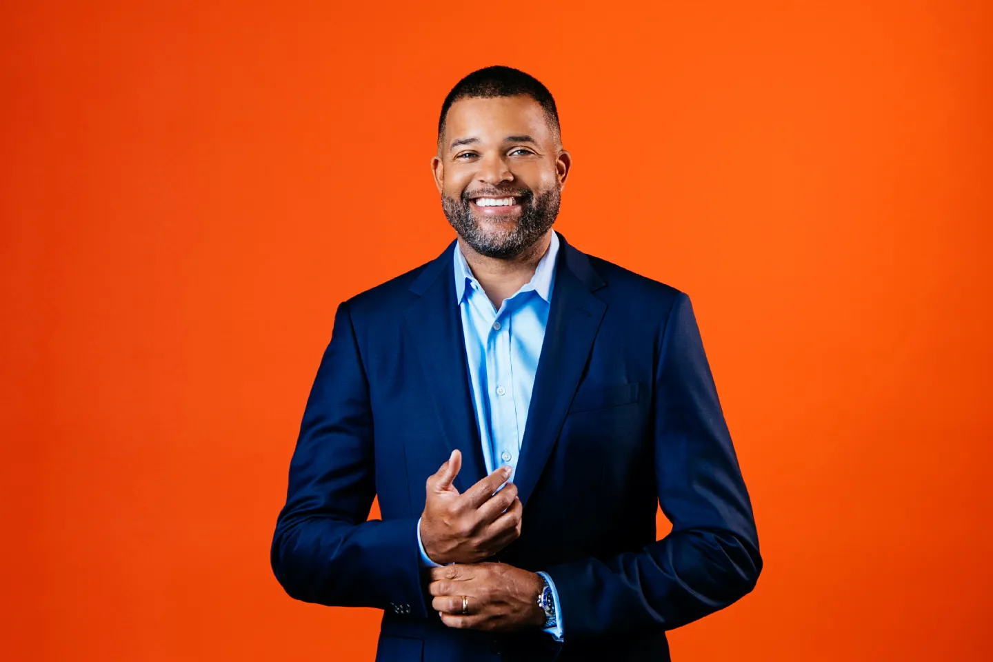 Man in a navy blue suit and light blue shirt against orange background.