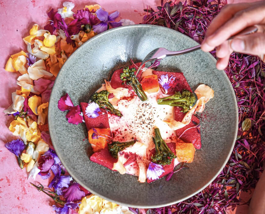 Plate of colourful food, broccolini, beetroot, squash creamy sauce and flower petals.