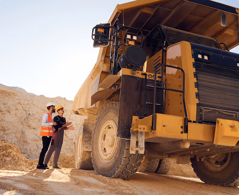 Two workers in safety gear using field service software beside a large yellow dump truck at a construction site