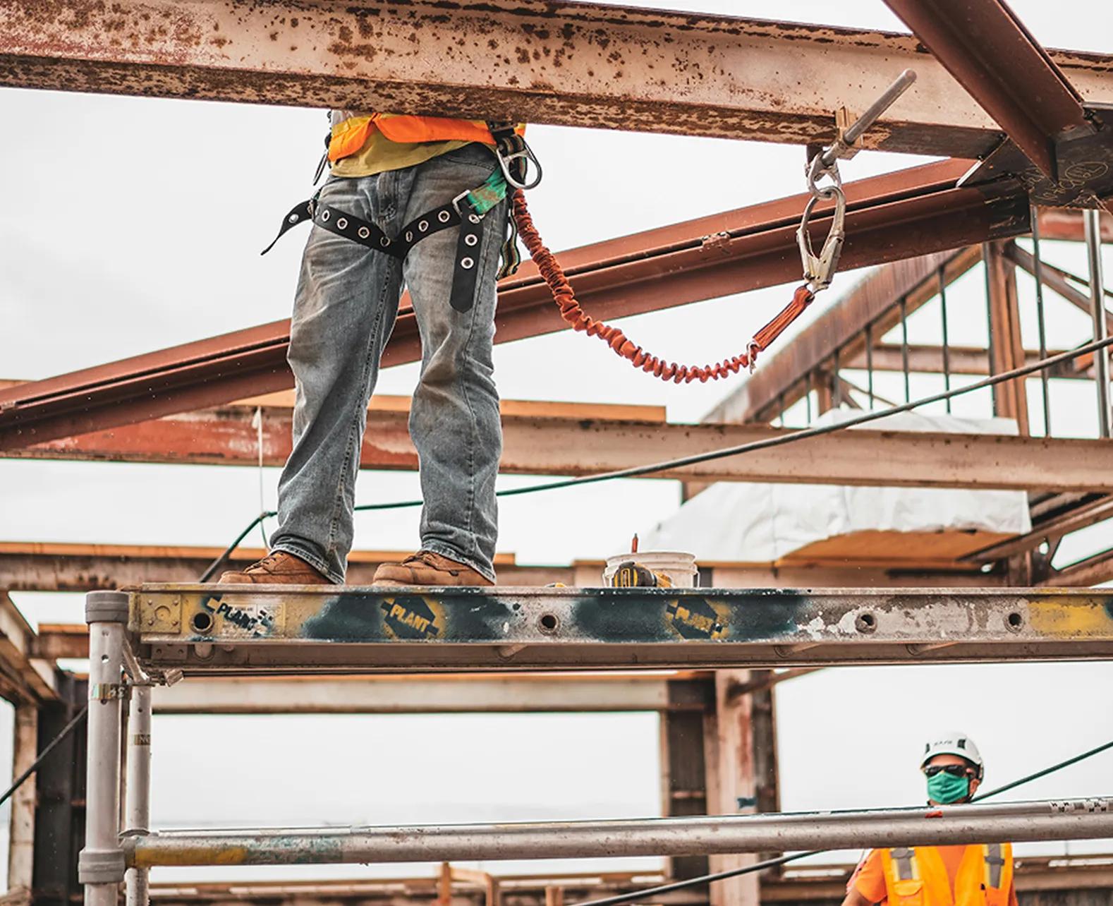 Two construction workers using Rux business apps and field service tools while working on a metal structure with scaffolding.