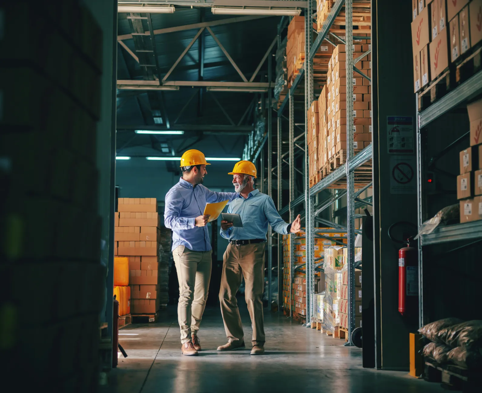 Two warehouse workers using Rux business apps and field service tools on a tablet, surrounded by shelves filled with boxes.