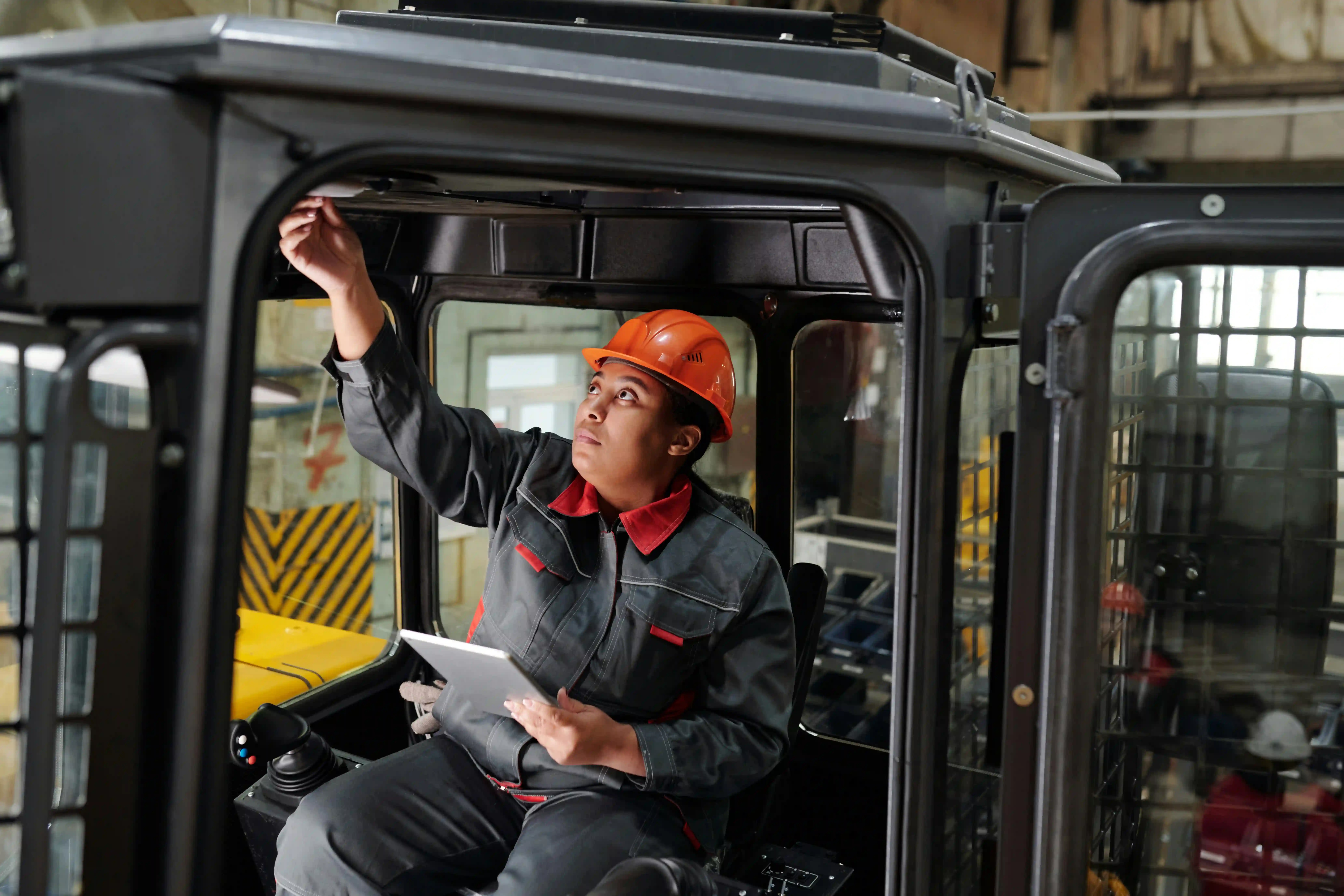 Construction worker using a tablet inside heavy equipment cabin on an industrial site 