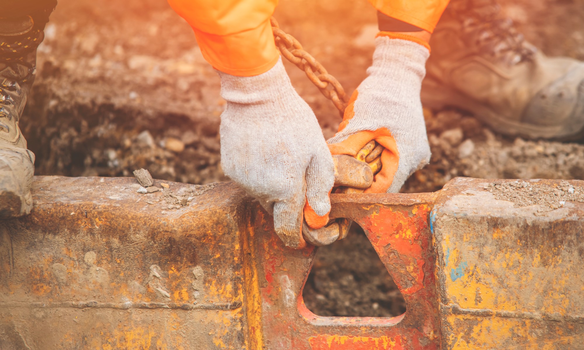 Worker securing trenching and shoring equipment with gloves and chain on a construction site, illustrating equipment rental tracking and vehicle and equipment tracking with RUX.