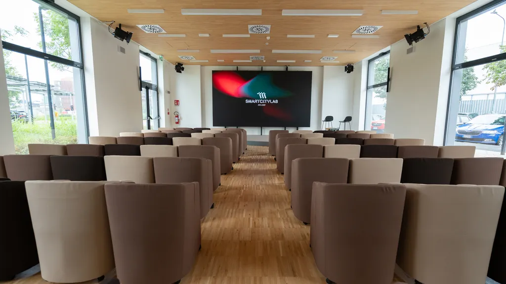 Sala conferenze moderna con sedie marroni e beige disposte in file di fronte a uno schermo con logo SmartCityLab.