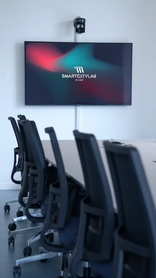 Sala riunioni moderna con sedie nere su ruote e grande schermo con logo SmartCityLab Milano.