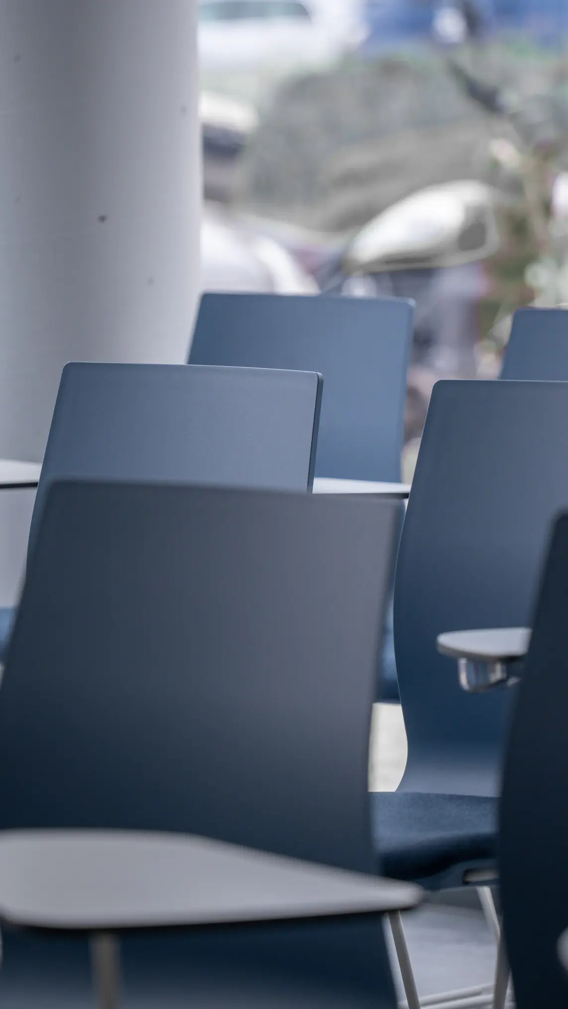 Sedie blu con piccoli tavoli attaccati in un ambiente interno vuoto.