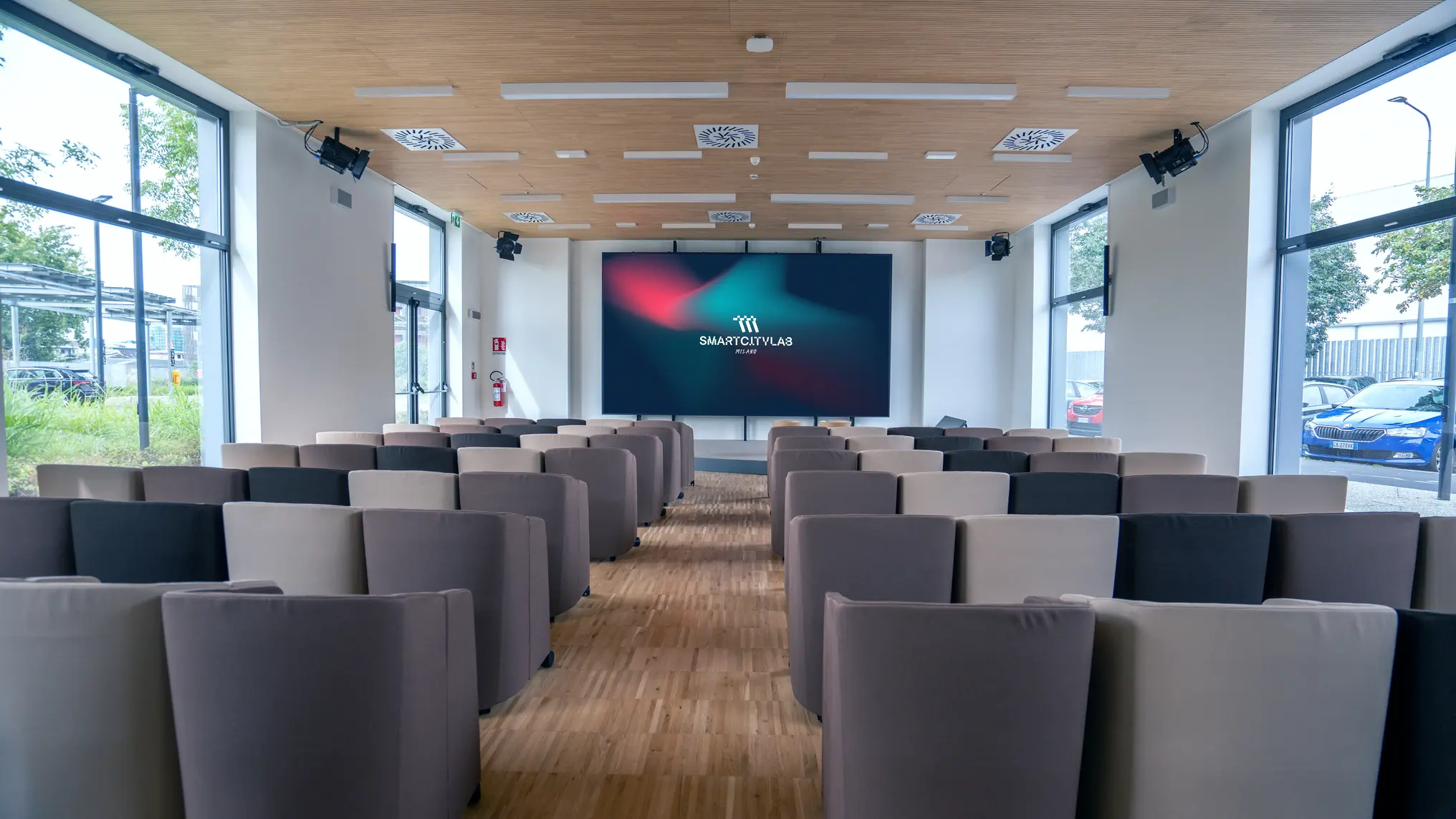 Sala conferenze moderna con sedie grigie e uno schermo grande con logo SmartCityLab Milano.
