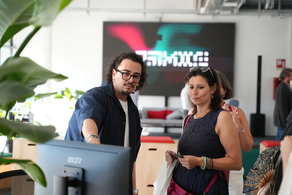 Due persone in ufficio guardano un monitor MSI mentre discutono, con una grande pianta a sinistra e uno schermo sfocato sullo sfondo.