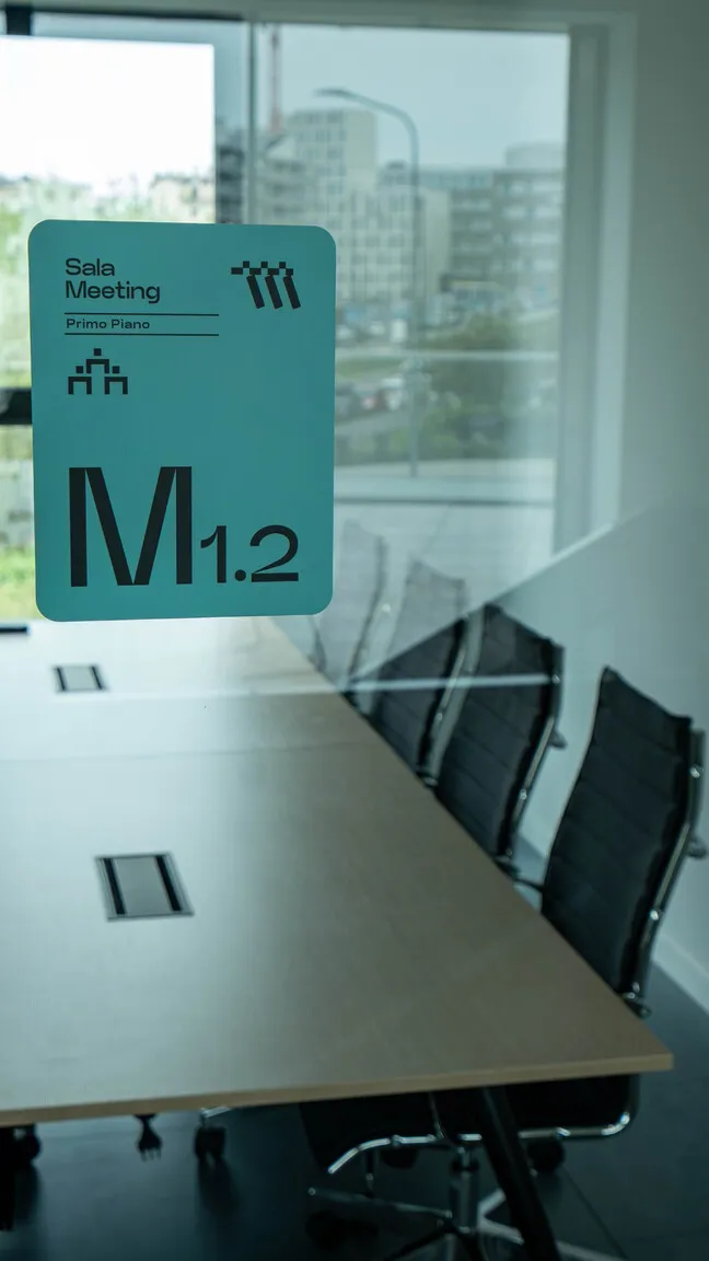 Sala meeting moderna con tavolo lungo, sedie nere e finestra ampia con vista su edifici urbani.