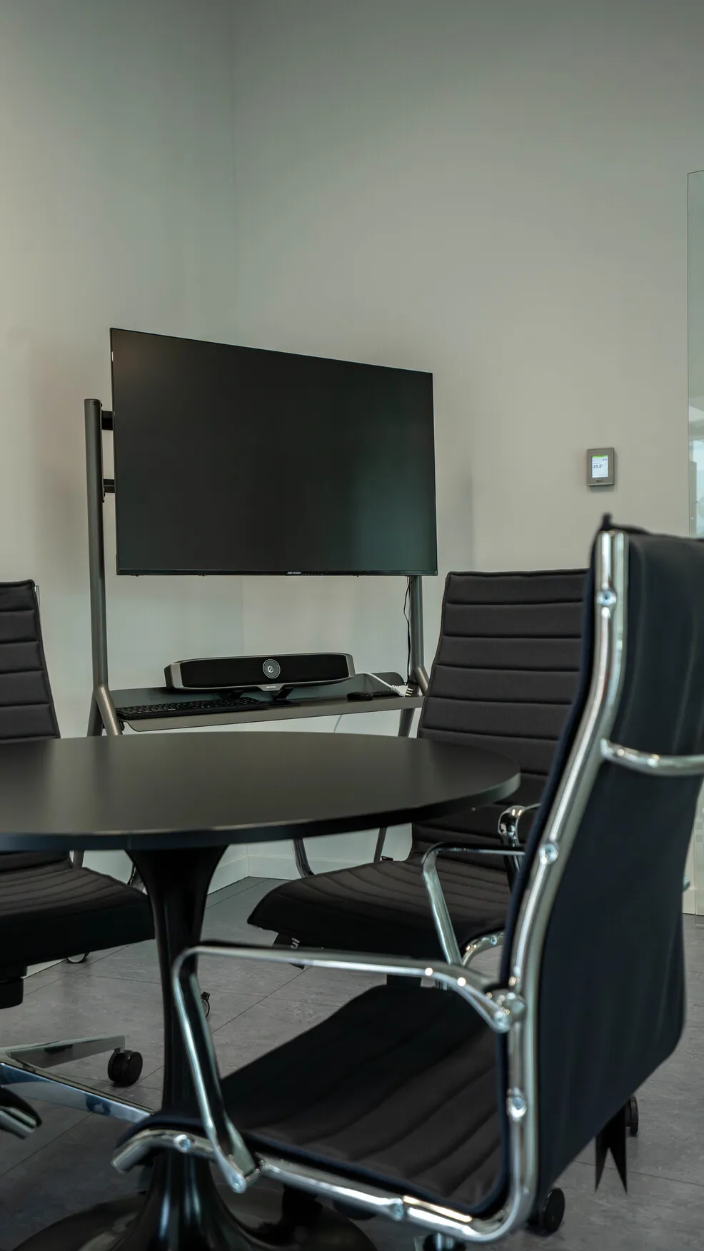 Sala riunioni moderna con tavolo rotondo nero, sedie da ufficio nere con braccioli in metallo e schermo TV su supporto.