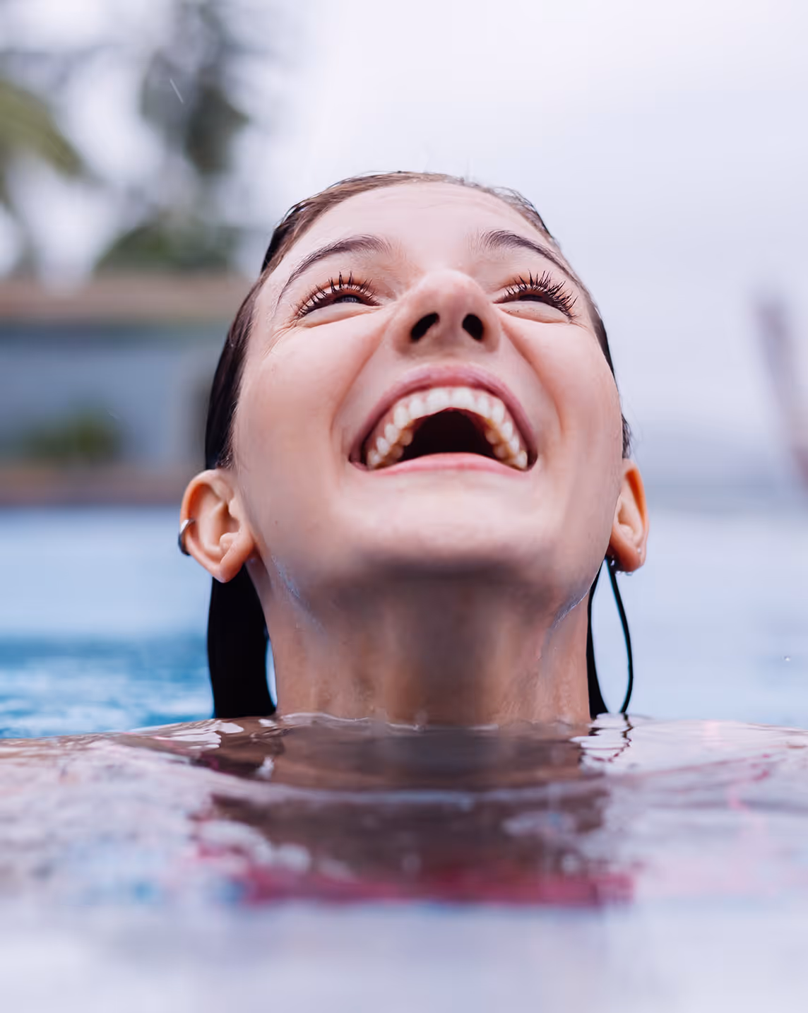 Close-up of a woman smiling and laughing with her head tilted back above water in a pool.