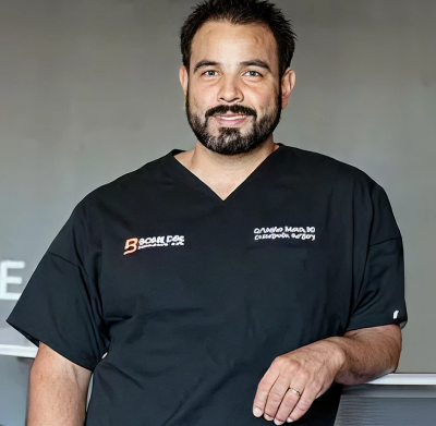 A man in a black scrub suit standing in front of a sign.