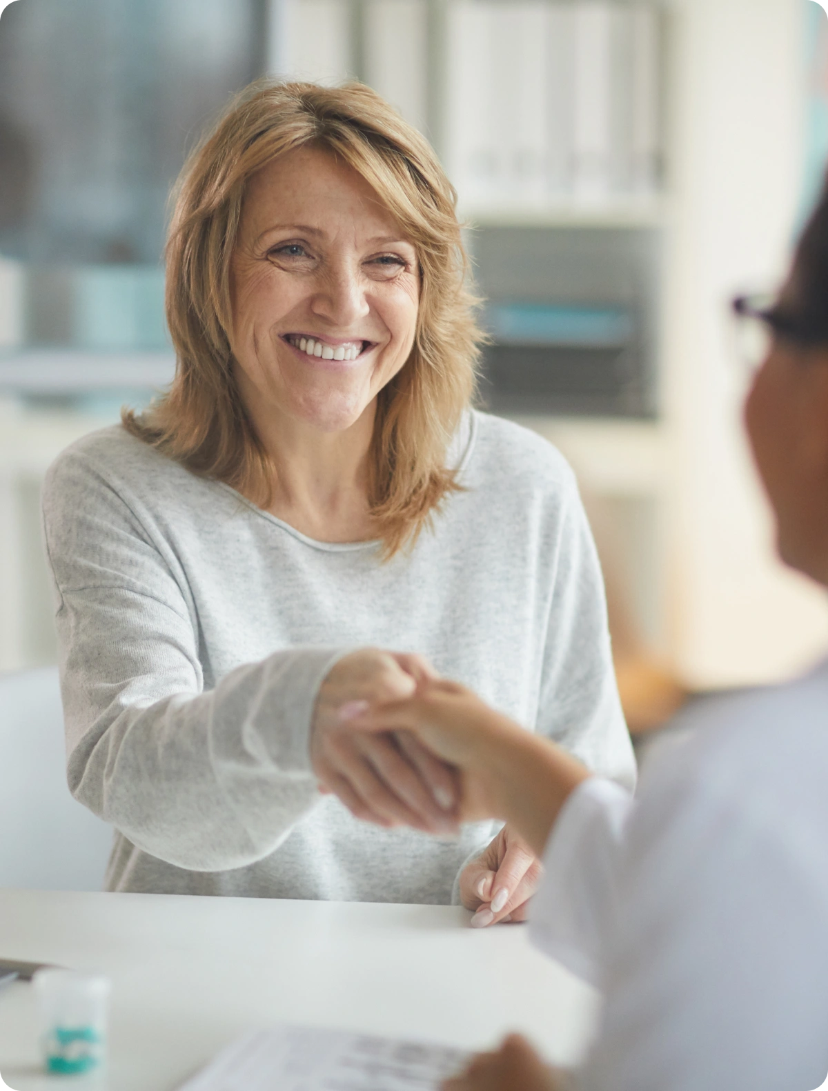 A woman shaking hands with another woman at a table.