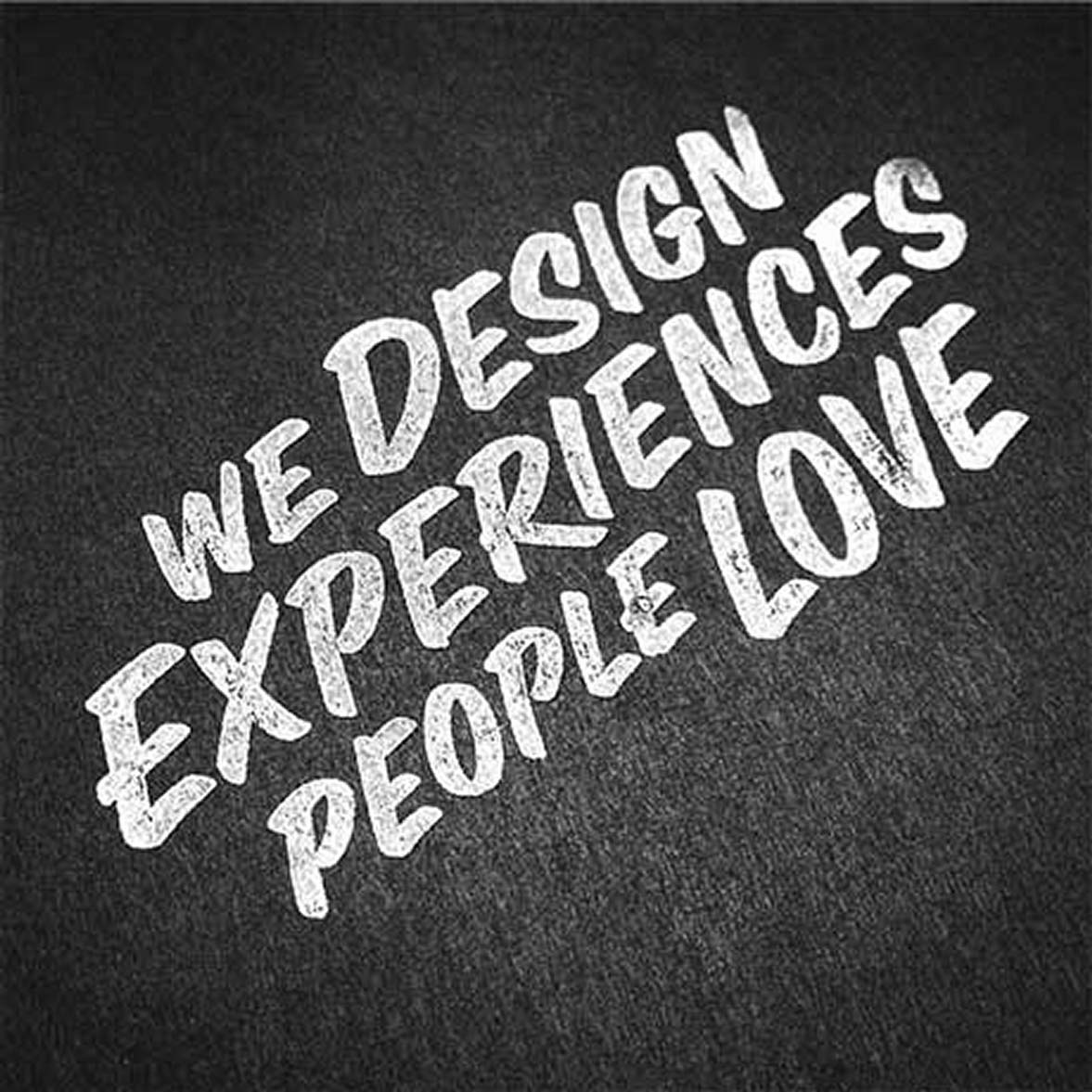 White chalk-style text on dark background reading 'WE DESIGN EXPERIENCES PEOPLE LOVE' arranged diagonally.