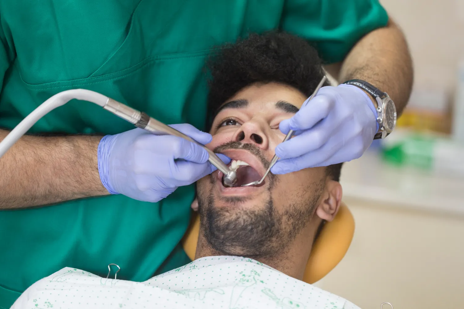 A male patient receiving dental care while reclining in a chair, as a dentist uses suction and instruments during the procedure.