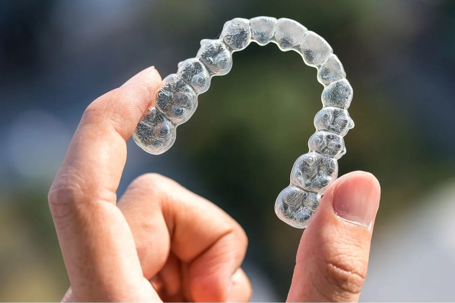 Close-up of a transparent clear aligner held between fingers, showing the molded upper dental arch for orthodontic use.