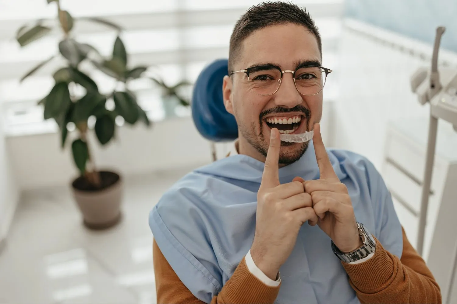 A cheerful male dental patient pointing to his teeth while smiling in a clinic chair, showing satisfaction with dental care.