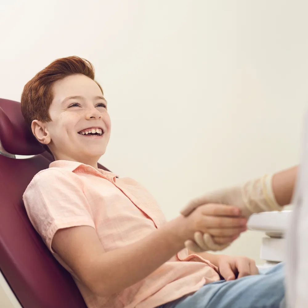 A red-haired boy laughing and enjoying himself while reclining in a dental chair.