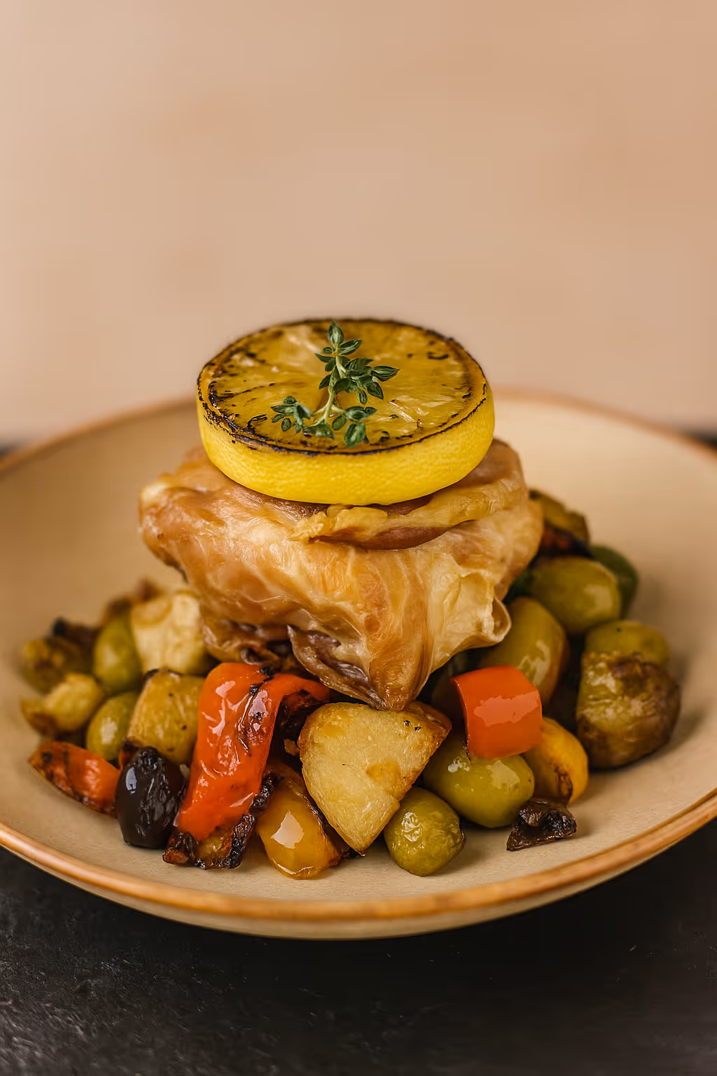 Gourmet dish featuring roasted vegetables topped with a pastry parcel and a grilled lemon slice garnished with fresh herbs.