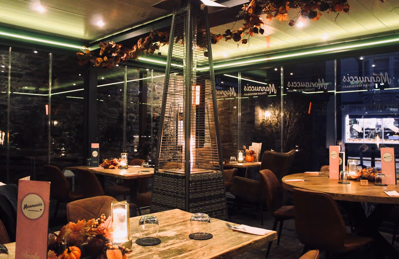 Cozy restaurant interior with wooden tables, autumn decorations, and a tall central patio heater.