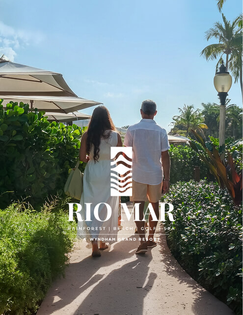 Couple walking through tropical gardens toward the beach at Wyndham Grand Rio Mar Rainforest Beach & Golf Resort in Puerto Rico.
