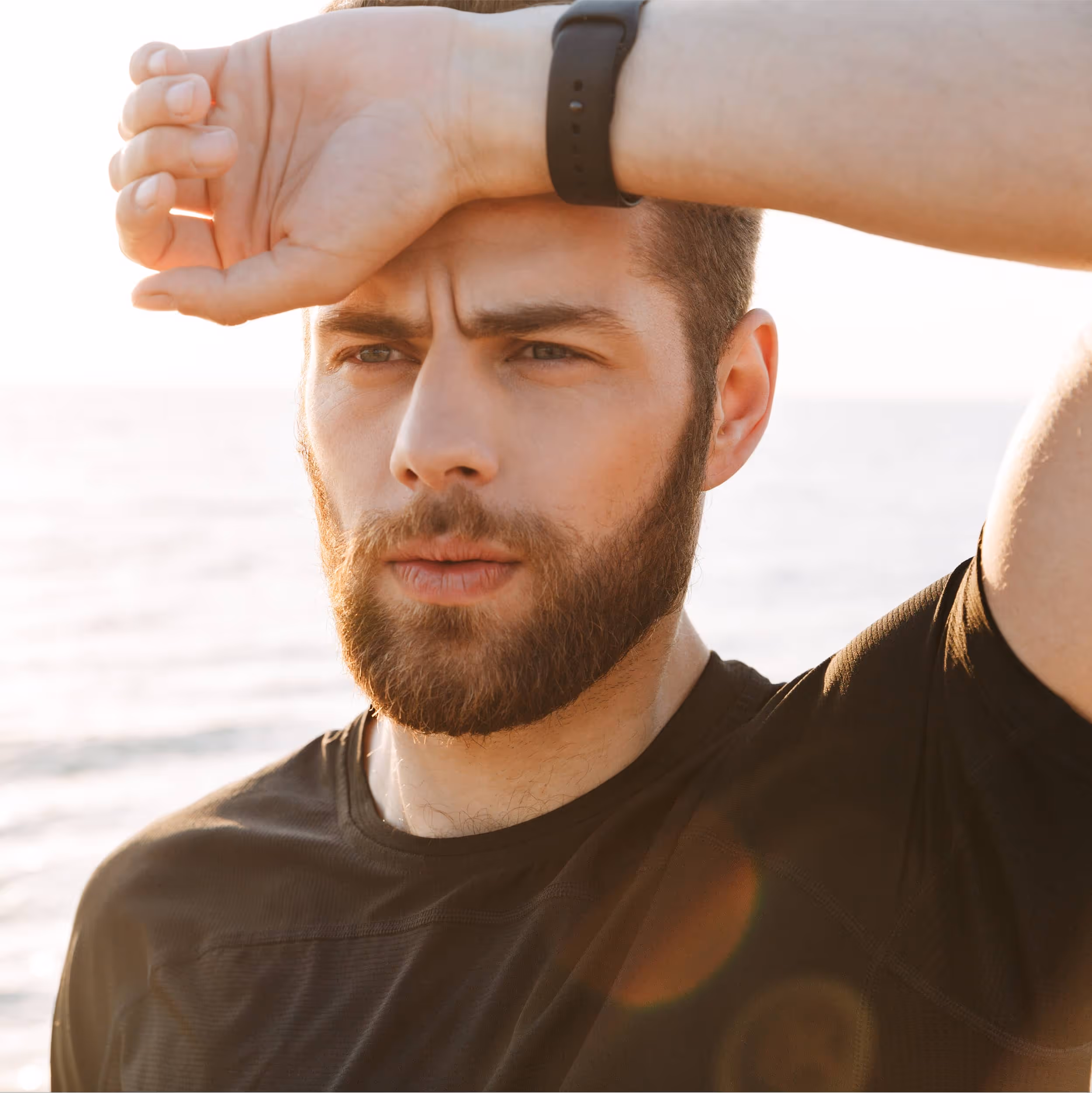 Man standing by the ocean with eyes closed, taking a deep breath in a calm and peaceful setting.