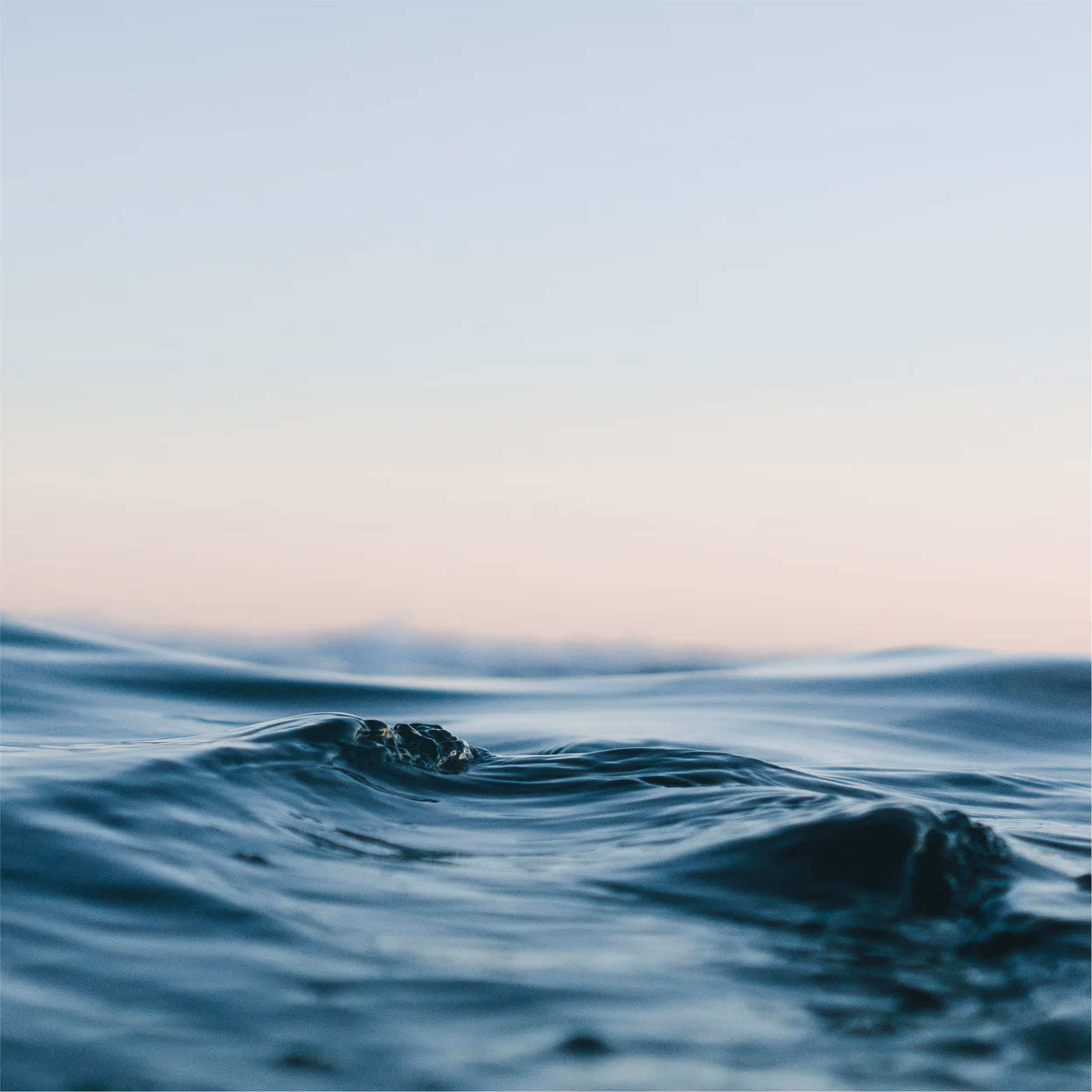 Gentle ocean waves during sunset with soft pastel sky.
