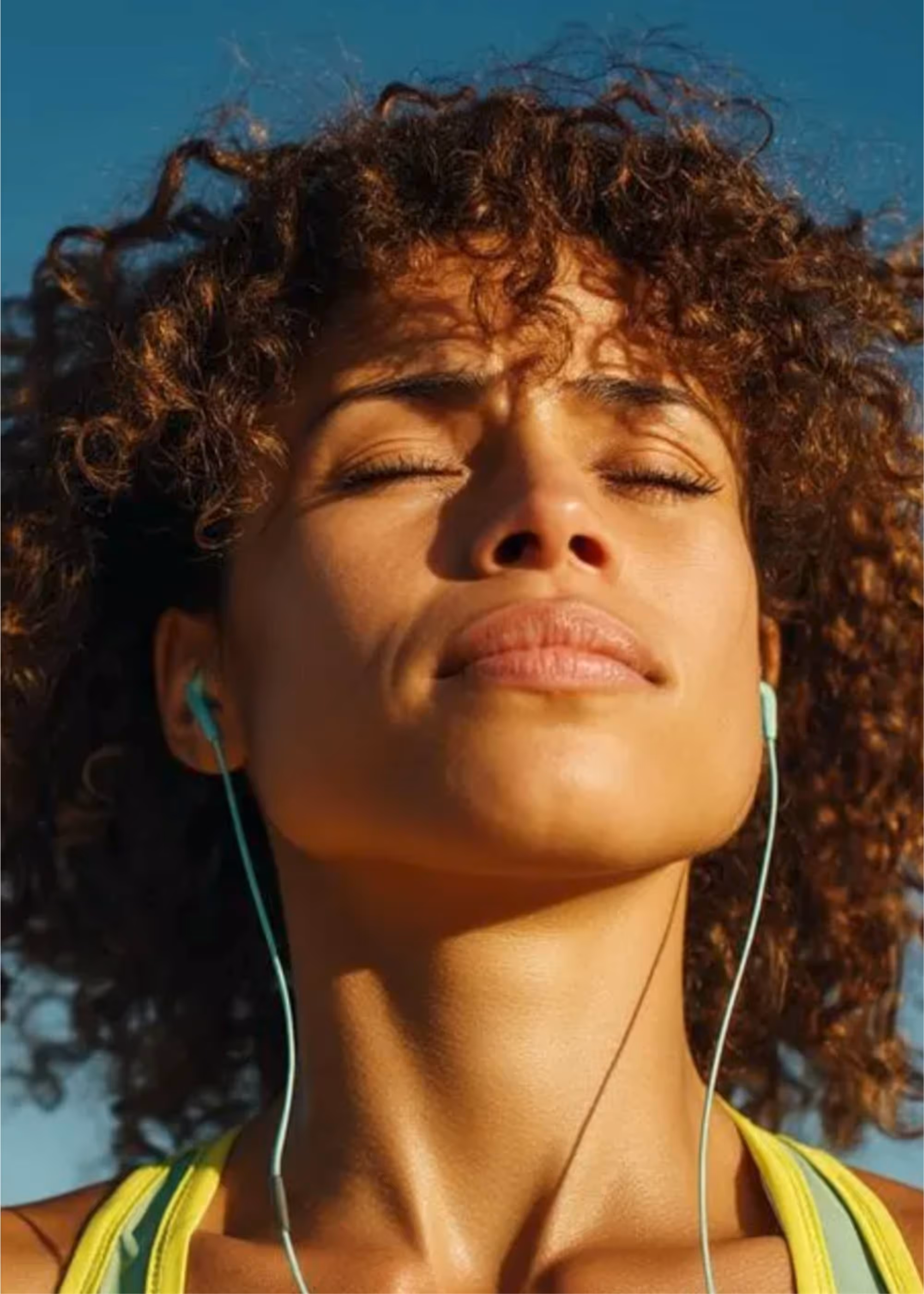 Woman using earbuds to take a mental reset in the sun, changing her conditions to regain focus.