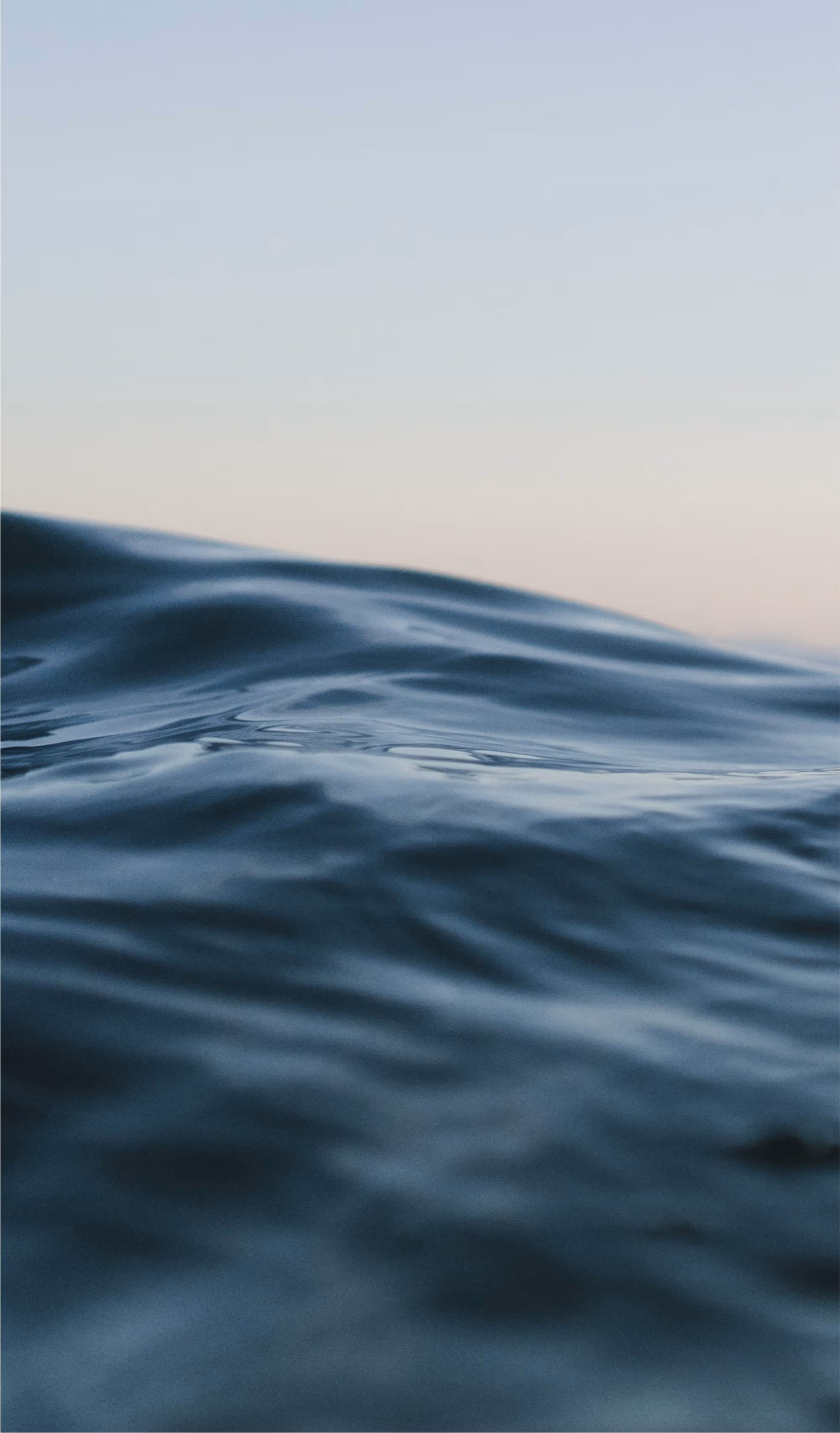 Calm ocean surface with soft ripples under a pastel sky at dusk.