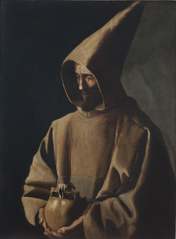 A man wearing a pointed brown hooded robe holding a human skull, illuminated against a dark background.