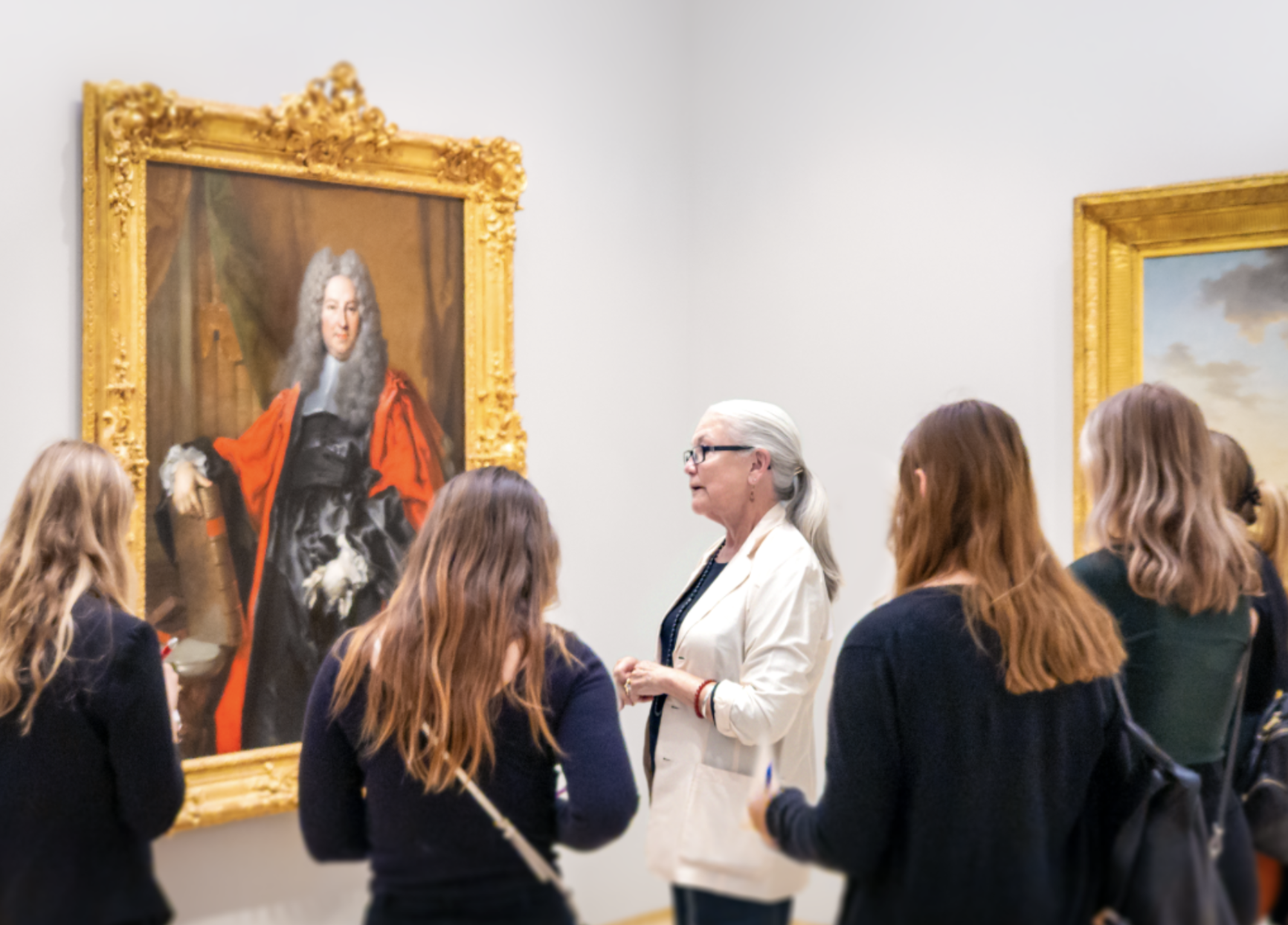 A group of people conversing in an art gallery with classical paintings on the walls.