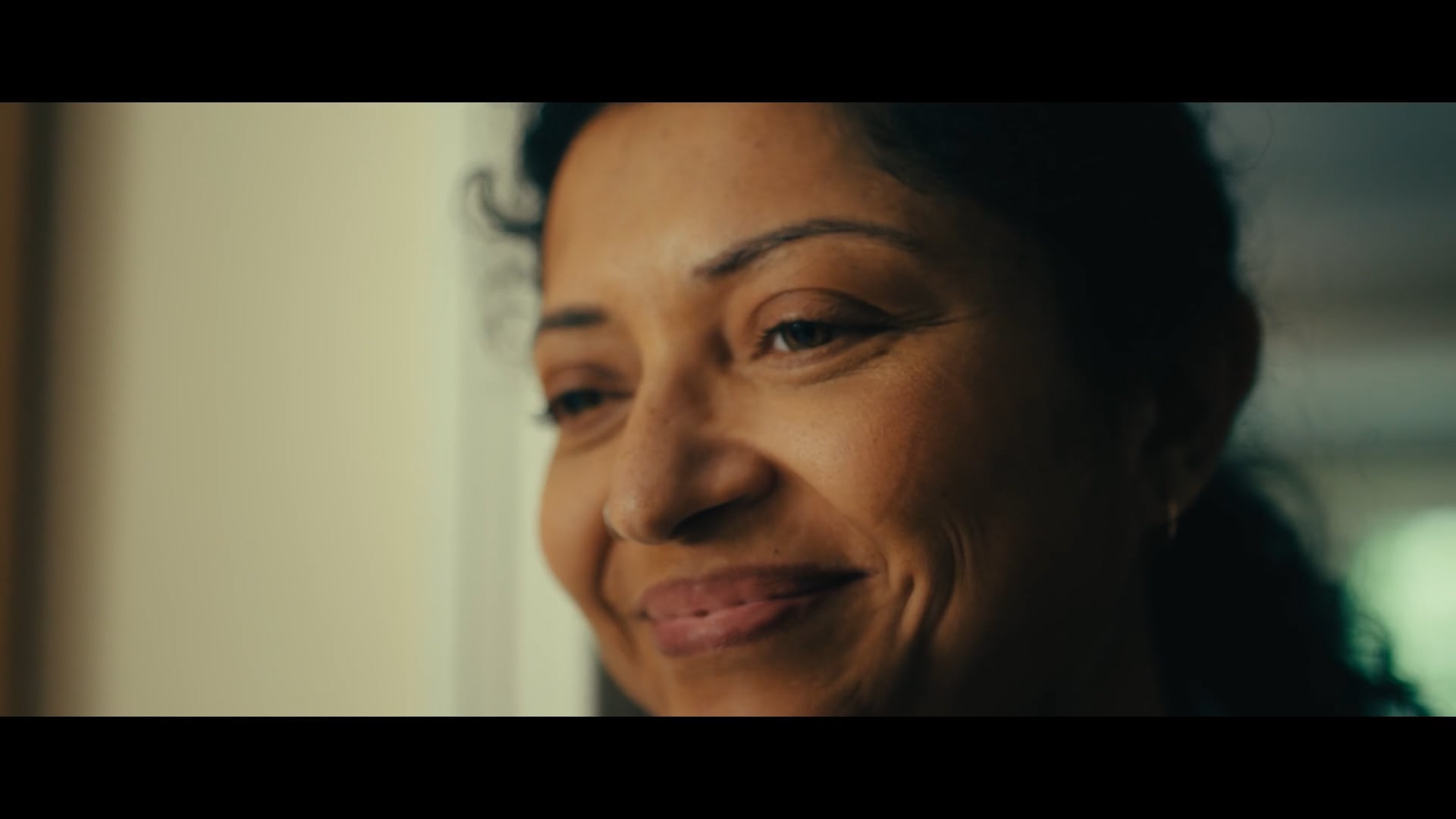A close-up of a woman smiling softly, her face warmly lit as she looks slightly to the side.
