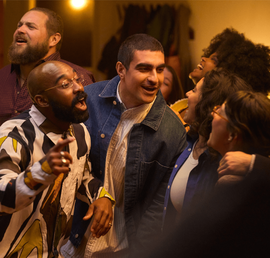 Five diverse adults laughing and interacting closely in a lively, dimly lit group setting.